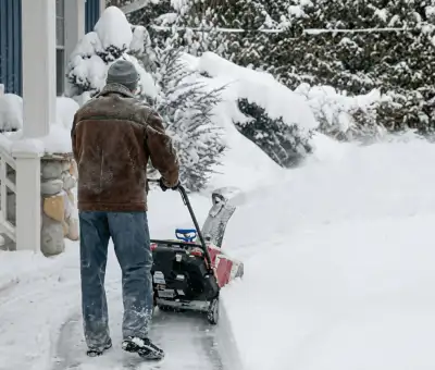 Residential snow removal technician using a snow blower to clear a home driveway and walkway in Des Moines, IA